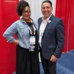 Joseph L. Soliz with a fellow attendee in front of a red and white trade show backdrop